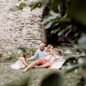 Photo de famille en provence devant un mur en pierres seches près d'Avignon. Une famille de eux enfants jouant au sol avec leur parent
