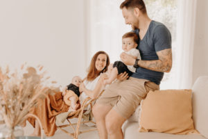 Jeunes parents assis avec leurs jumeaux dans les bras. Seance photo de famille près d'Avignon, provence. Leurs vetements sont différents mais harmonieux