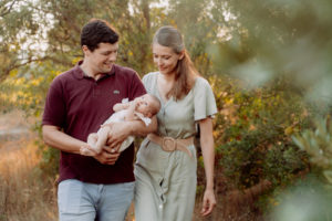 Un jeune couple de parents se promenant avec leur nouveau-né dans la campagne provencale. Ils son thabillés avec des couleurs complémentaires et des vêtements qui s'accordent sans être similaires