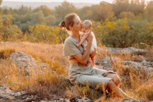 Une mère qui embrasse son bébé, durant le coucher du soleil en Provence. Elle porte une robe fluide et de couleurs pastels. Robe aux couleurs clairs et pastel